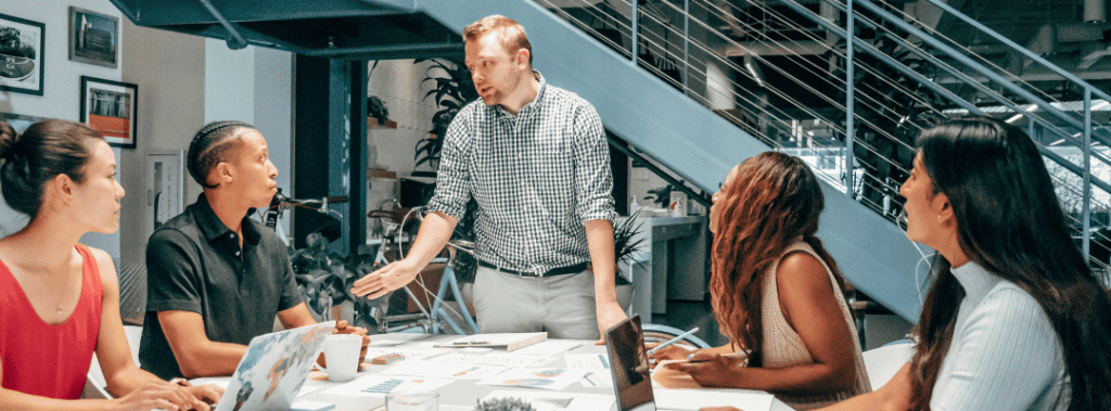 Man Leading a Meeting With Employees Sitting Around Table